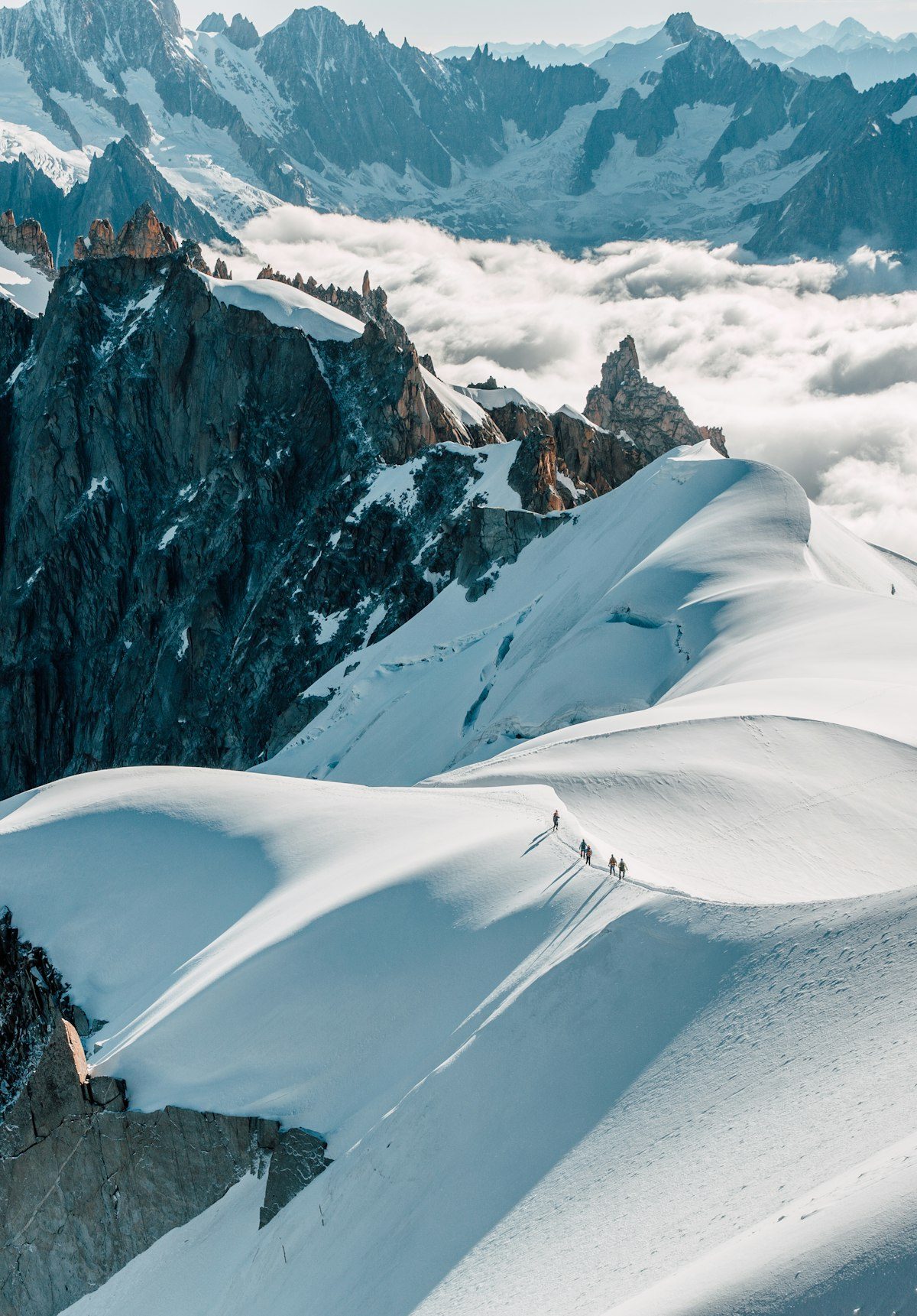 Une cordée sur une arête enneigée, au-dessus d’une mer de nuages