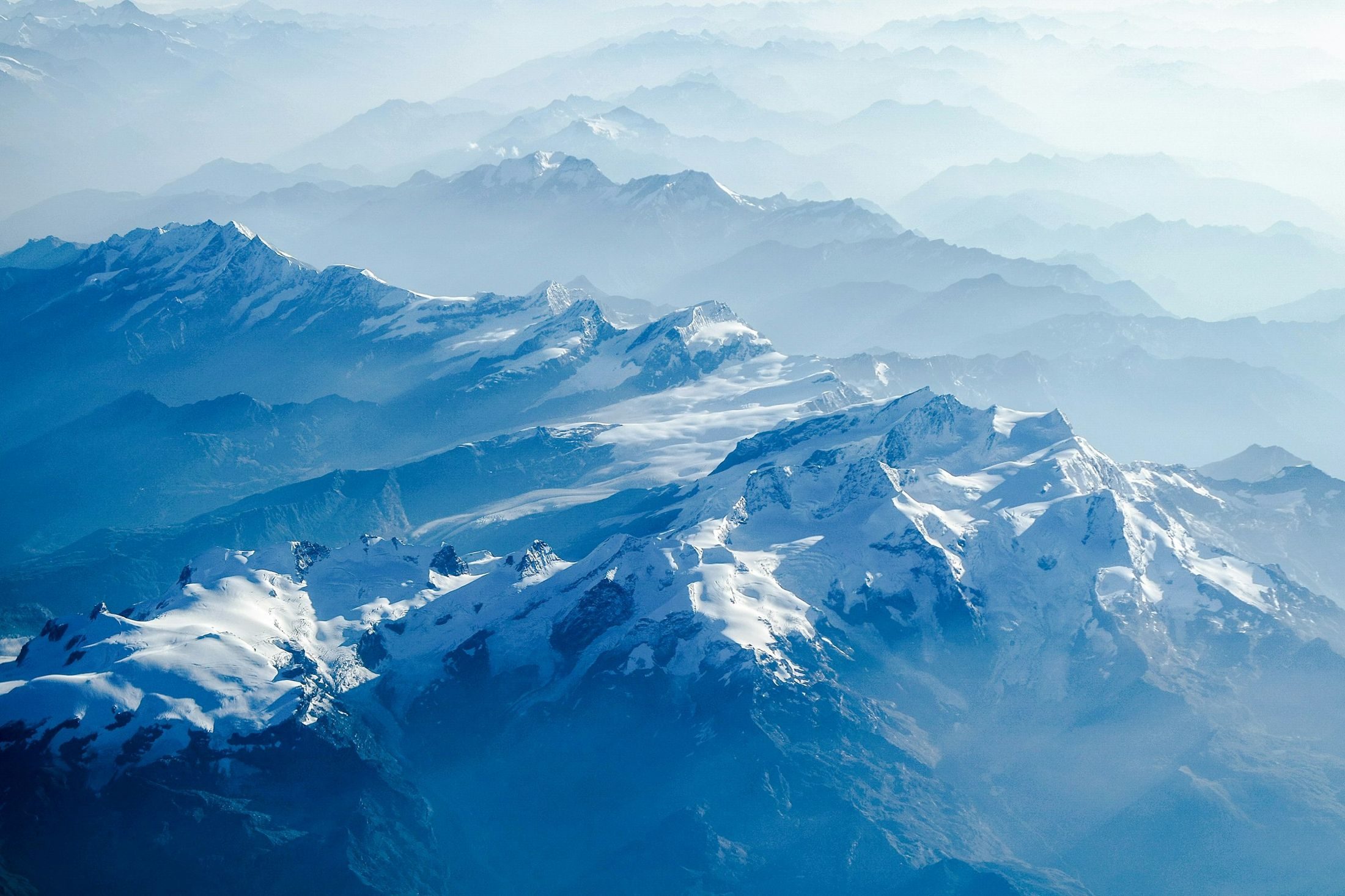 Massifs enneigés et vallées dans la brume, vus du ciel